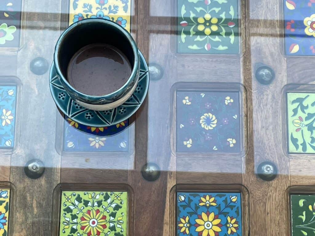 A blue cup of coffee on a multicoloured tiled table