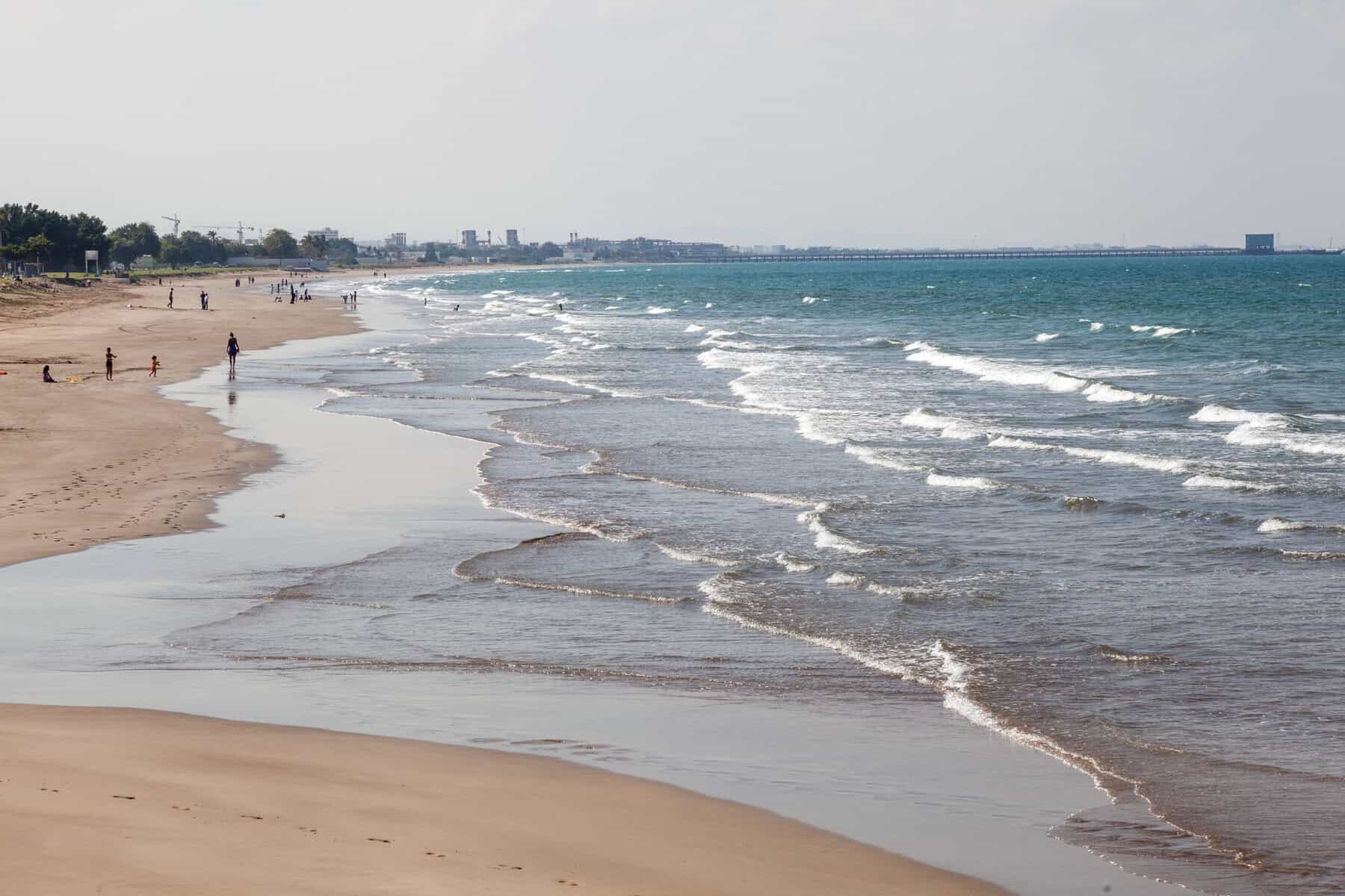 Al Qurum Beach in Muscat with gentle waves rolling onto a wide sandy shoreline