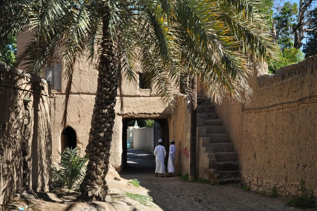 2 Omani men wander among the mud houses in Birkat al Mouz, Oman