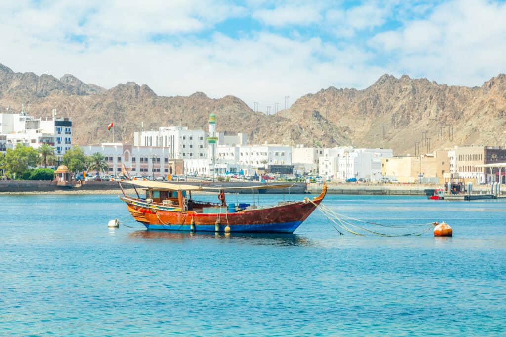 Mutrah promenade panorama with mountain range and sea gulf with anchored traditional dhow boat, muscat.