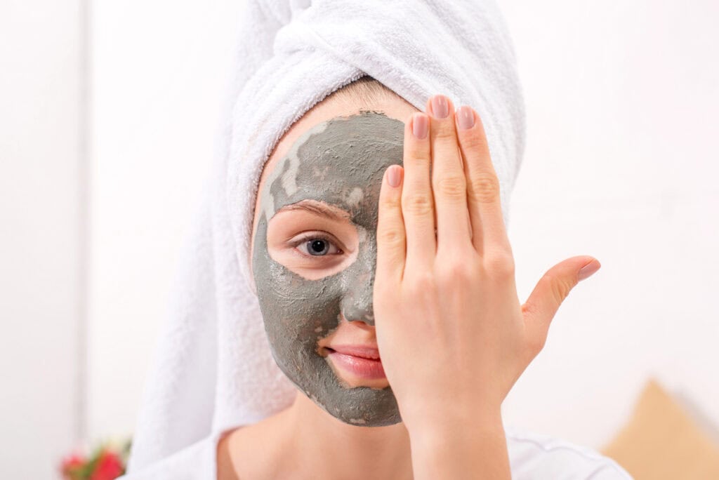 A young woman with a towel on her hair and clay mask on her face