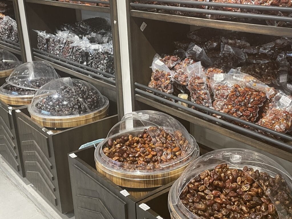 A display of Omani dates in large round containers with clear lids, surrounded by shelves filled with packed dates in different varieties.