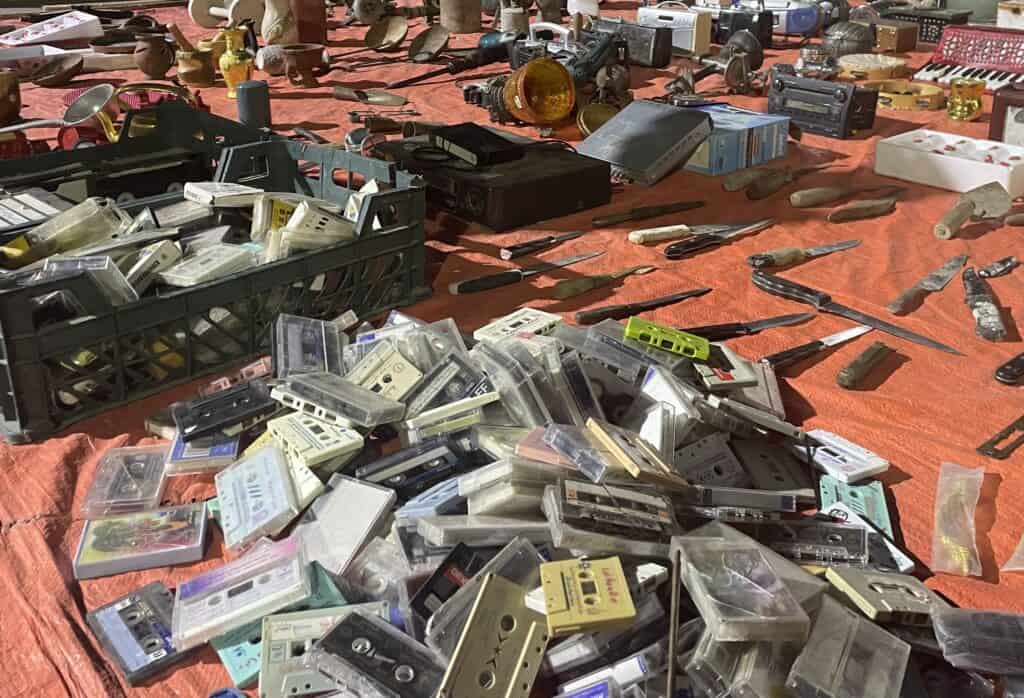 Assortment of old cassette tapes, tools, and second-hand objects laid out on a sheet at Nizwa Souq’s outdoor market corner
