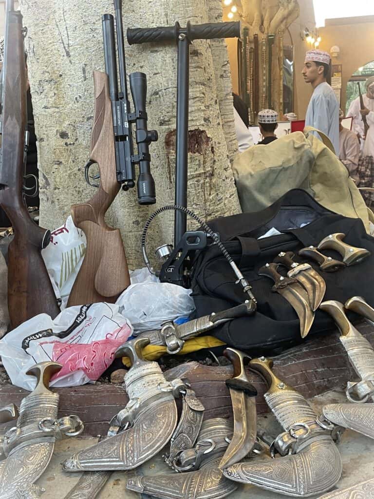 Display of Omani khanjars, rifles, and tools laid out for sale at the Nizwa Souq arms market during the Friday auction.