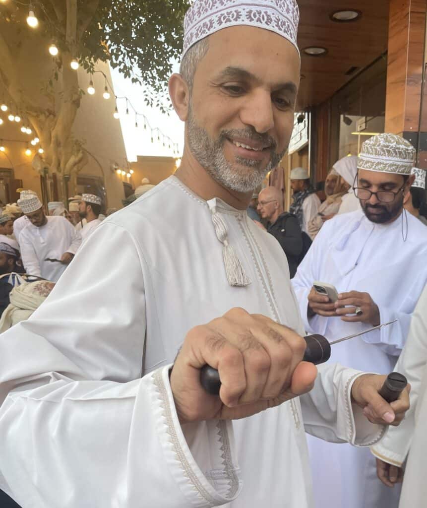 A man smiling and holding a newly purchased knife at the arms market in Nizwa Souq