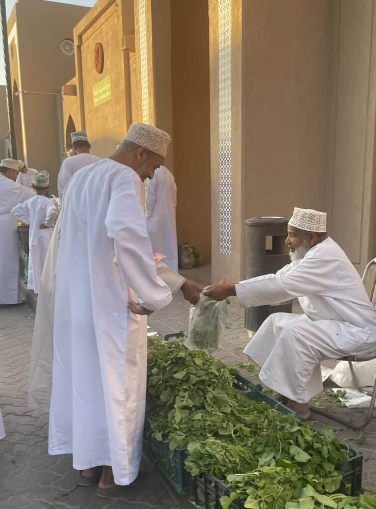 Omani vendor handing a bag of fresh greens to a customer at the vegetable souq in Nizwa.