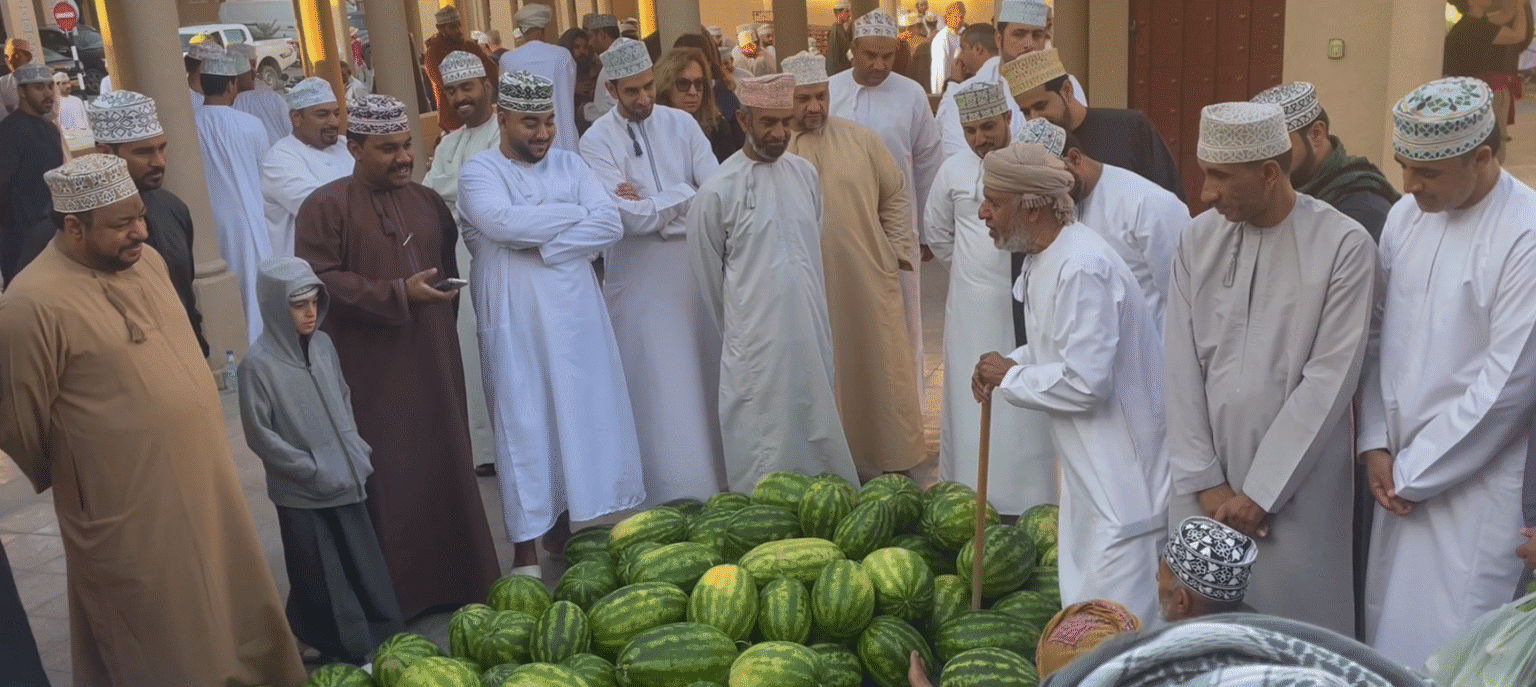 Men gathered around a pile of watermelons at Nizwa Souq in Oman during the Friday market