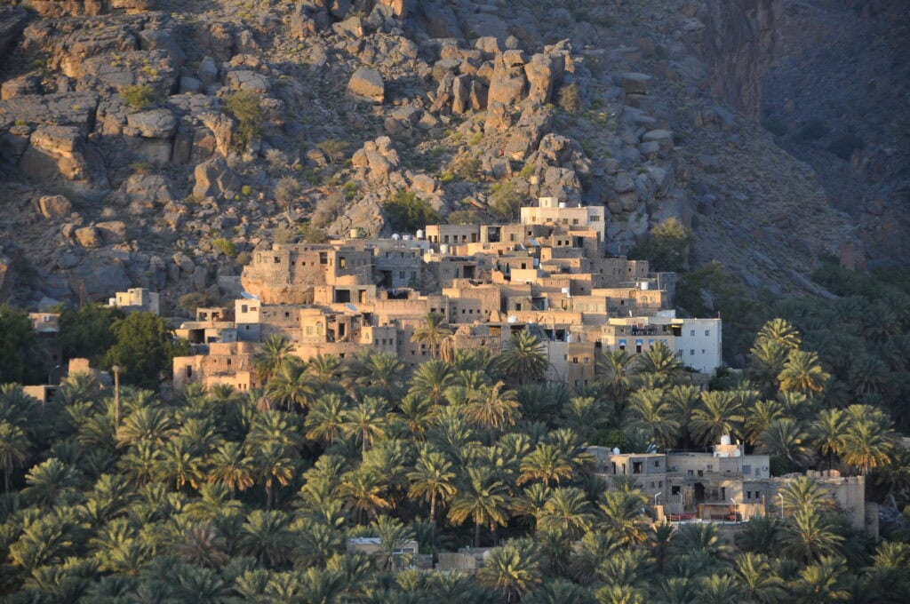 Aerial view of Misfat al Abriyeen, a traditional Omani mountain village built from stone and surrounded by dense date palm gardens.