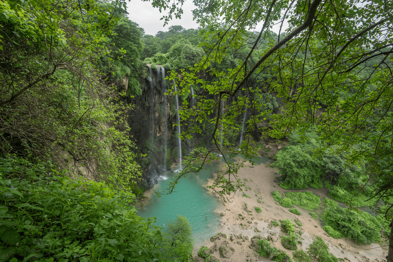 Waterfall flowing into a turquoise pool surrounded by lush green vegetation in Salalah
