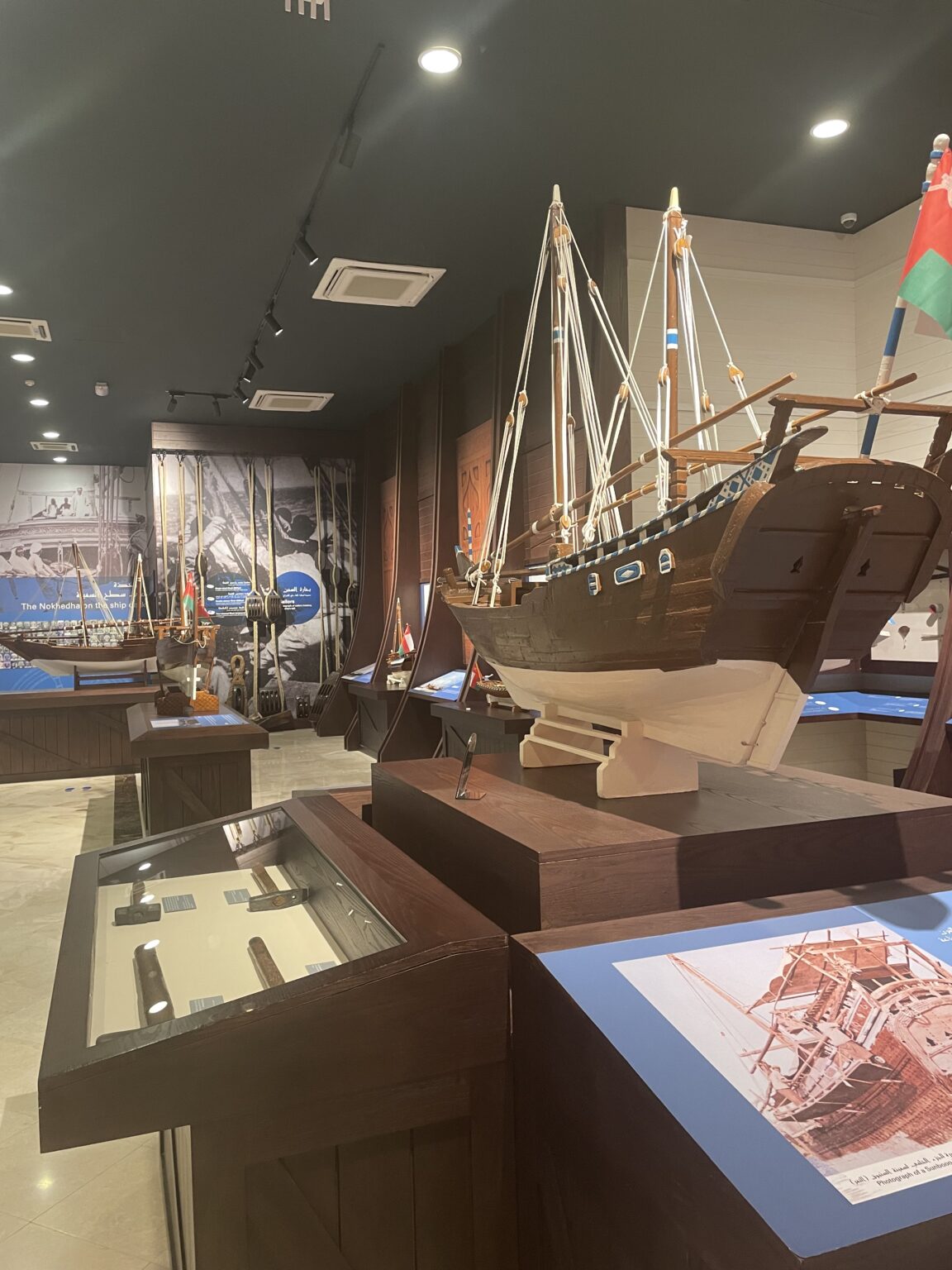 An interior view of the Sur Maritime Museum showcasing a large, detailed wooden model of a traditional Omani dhow with intricate rigging.