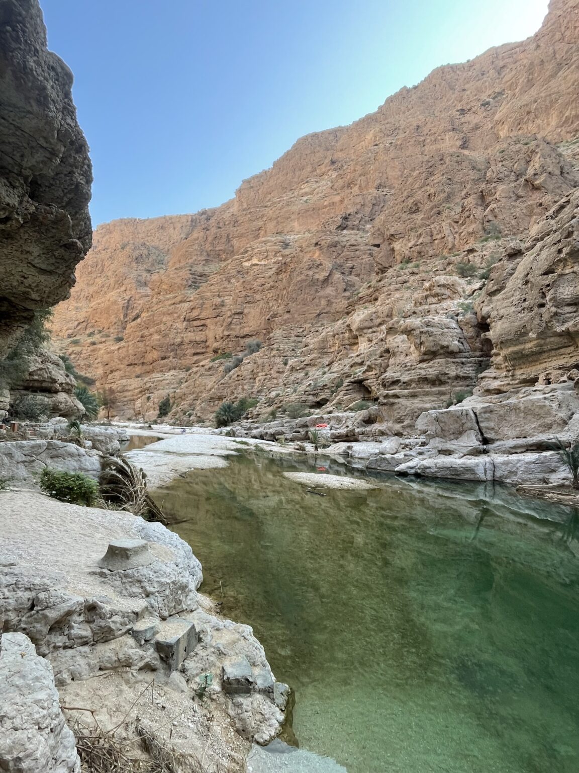 Emerald pools and towering canyon walls at Wadi Shab, Oman, with crystal-clear water reflecting the dramatic landscape